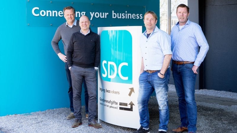 Vier mannen staan voor een bord met de tekst SDC.