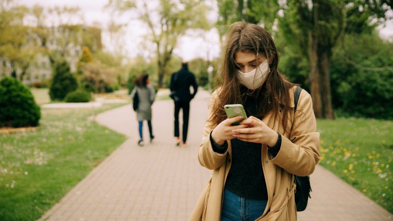 Een vrouw met mondkapje gebruikt haar telefoon in een park om toegang te krijgen tot de CoronaMelder-app.